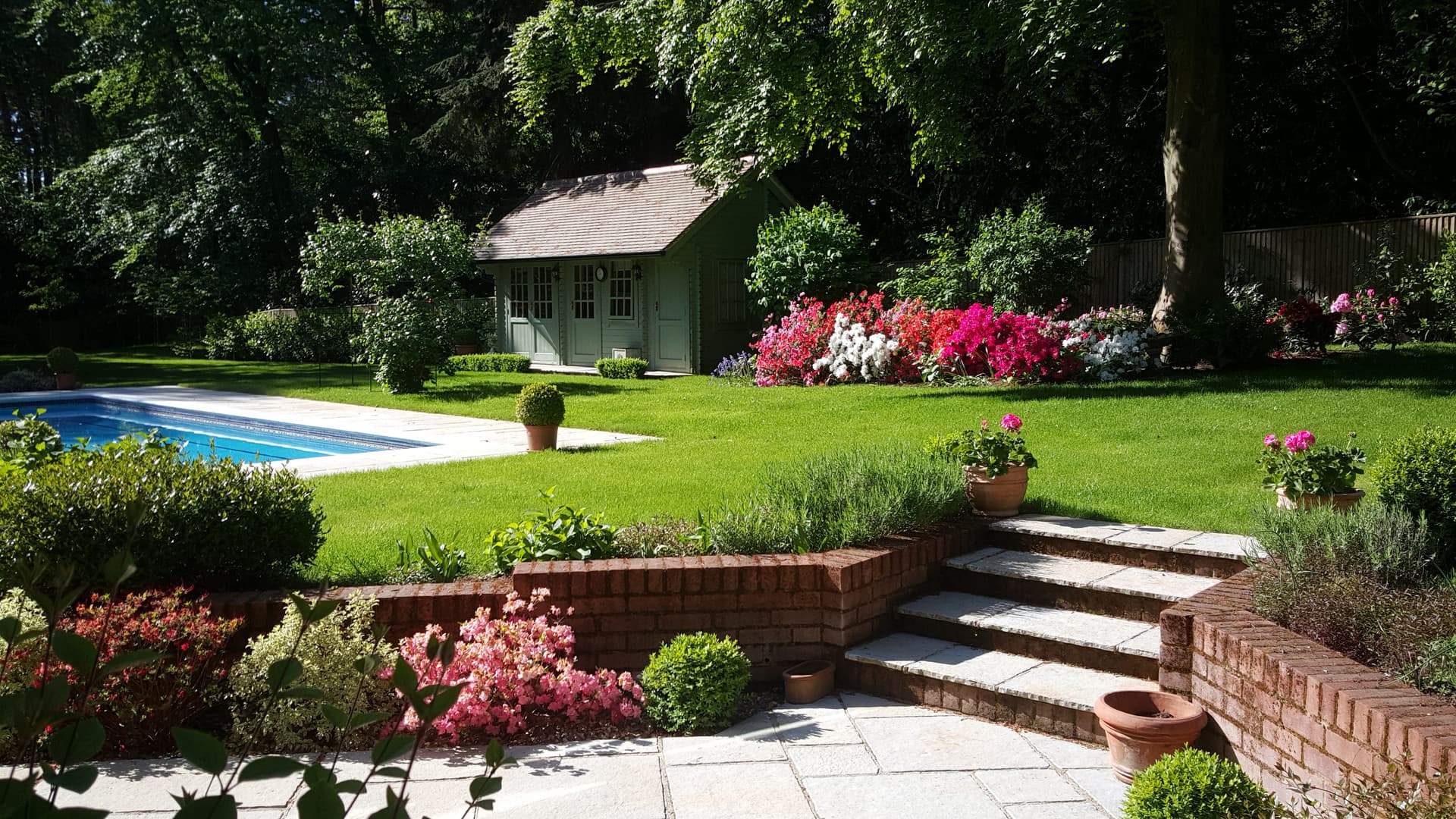 A landscaped garden with pool house, lawn and brick steps designed as an extension of the house